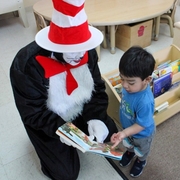 A person dressed as the Cat in the Hat shares a picture book with a young child who points to an illustration.