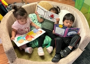 Three young children sit together on a couch, each looking through a different picture book.