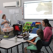 A Meridian School educator leads a group reading activity using a projected picture book while a student follows along on a laptop.